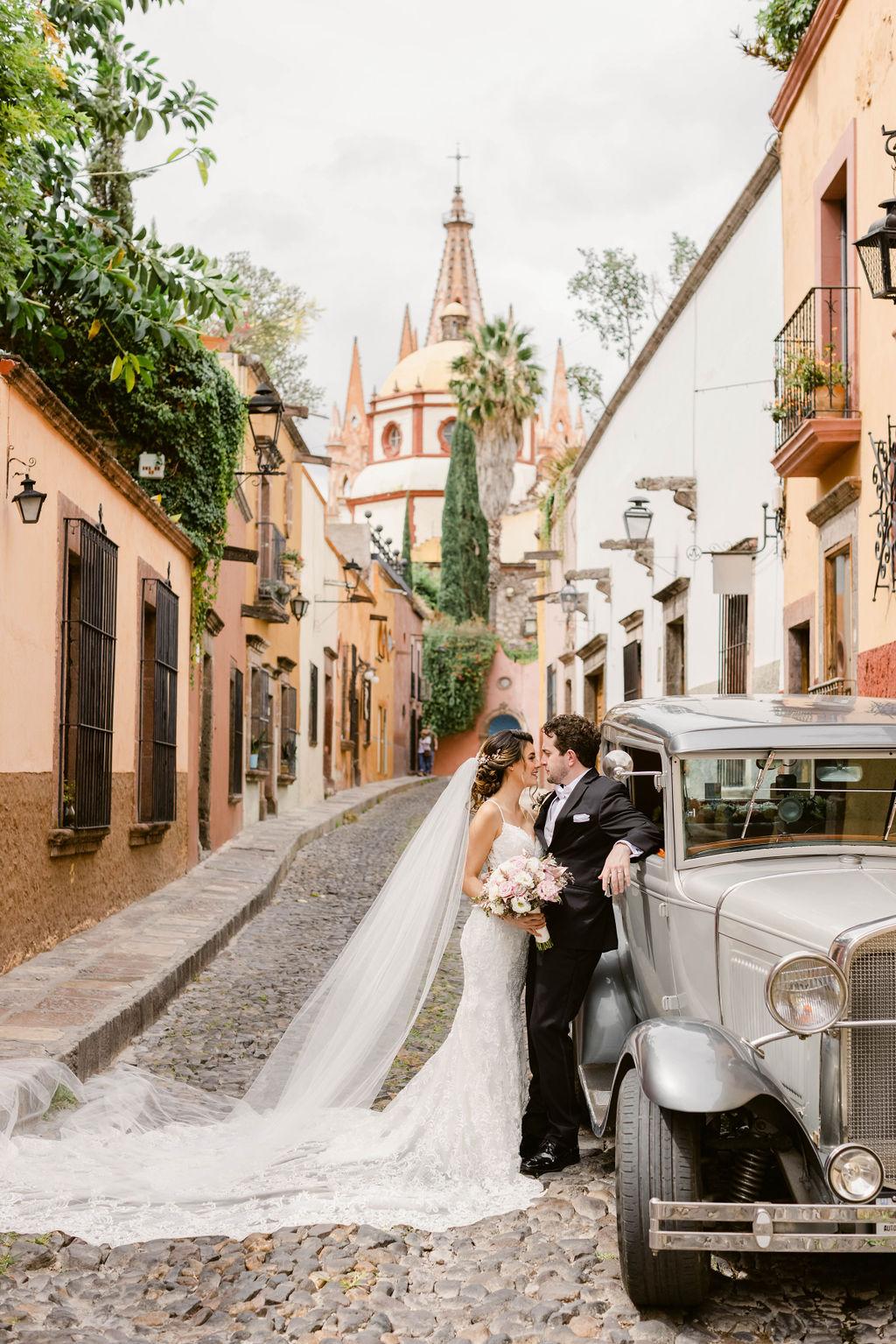 Couple with the Parroquia and vintage car on cobblestone streets